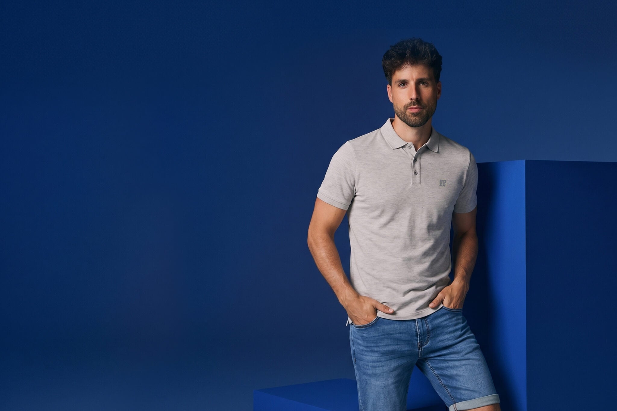 Man wearing a gray polo shirt and blue jeans against a blue background